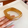 Amber marble square resin bangle held by hand, showing translucent swirl texture - Light Coffee