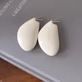 Primo piano di orecchini a goccia color crema minimalisti lucidi su un libro grigio - Bianco
