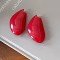 Primo piano di eleganti orecchini a goccia rosso vibrante su sfondo grigio minimalista - Rosso
