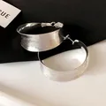 Primo piano di grandi orecchini a cerchio argento con texture spazzolata e design geometrico - Argento
