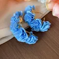 Close-up detail of light blue chiffon fabric flower C-shaped hoop earrings on wood. - Silver Earring Post Style / Gold-Blue