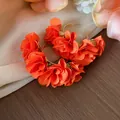 Close-up detail of vibrant orange chiffon flower C-shaped earrings on a silk background. - Silver Earring Post Style / Gold-Orange