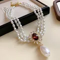 Vue détaillée d'un collier de perles à trois rangs avec fleur en cristal rouge et goutte - Collier-Or-Blanc-Rouge