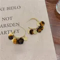 Close-up detail of stylish tortoiseshell and gold tassel hoop earrings on linen cloth - Gold with Coffee