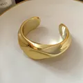 Vista macro detallada de un brazalete abierto dorado pulido con diseño irregular. - Dorado