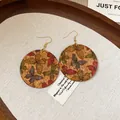 Close-up of cork drop earrings featuring colorful butterfly prints and gold hooks - Colorful Butterfly Style / Coffee