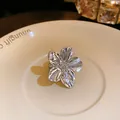 Primer plano detallado de un anillo abierto con forma de flor plateada en un plato - Diseño de Flor (HR1510) / Plateado