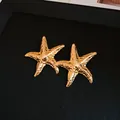 Macro view of gold starfish stud earrings featuring a detailed hammered metal texture - Gold
