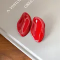 Vista detallada de pendientes de botón rojos irregulares de esmalte sobre un libro. - Óvalo Irregular (HE28177) / Rojo