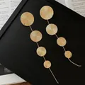 Close-up of gold tiered disc tassel earrings on a textured black background frame. - Silver Pin Tassel Style / Gold
