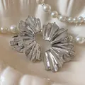 Close-up detail of silver metallic flower fan-shaped pleated earrings on a pearl background. - Silver