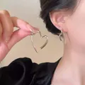 Nahaufnahme von minimalistischen herzförmigen Creolen in Silber am Ohr einer Frau getragen - Herzform Stil