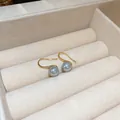 Detail shot of gold-plated hook earrings with elegant grey pearls in a soft jewelry box. - Grey Pearl Ear Hook 8mm (Ear Hook)