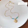 Detail view of golden stainless steel sun necklace with blue bead pendant on white plate - Sun Evil Eye Style / Gold with Blue