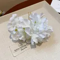 Close-up detail of white fabric flower hair pin with U-shaped gold metal fork. - White