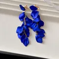 Close-up of cobalt blue pleated petal tassel earrings on a white display base - Clip-on Earrings / Purple