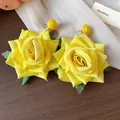 Detalle de pendientes de rosas de tela amarilla con base de rafia y detalles de hojas verdes. - Pendientes de Botón (HE30753) / Amarillo