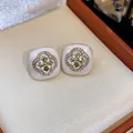 Detailed macro view of elegant square enamel flower stud earrings with sparkling zircon halo - Cross Flower Style / Gold-Beige