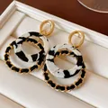 Close-up of geometric round dangle earrings with gold chain and black marble resin - Gold-Black