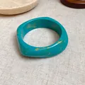 Close-up of a retro turquoise resin square bangle with elegant yellow marble patterns. - Blue