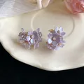 Detail view of sweet purple flower earrings with pearl centers on a cream plate. - Purple