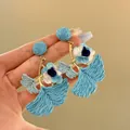 Detailed view of the blue raffia texture and fabric flower on these ginkgo leaf earrings - Blue