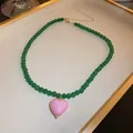Close-up of a green beaded necklace featuring a glossy pink heart pendant on a tray - Green Heart Necklace (8) / Green