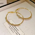 Primer plano de pendientes de aro dorados con strass pavé y detalle de cruz - Aro Grande con Cruz de Estrás / Dorado