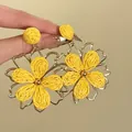 Gros plan détaillé de boucles d'oreilles fleur en raphia jaune avec cadre doré - Style Floral 3D (7#)