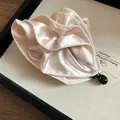 Dettaglio macro del design a fiore in tessuto satinato plissettato su un fermaglio beige - Clip a Torsione / Bianco