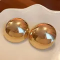 Close-up of gold-toned oversized dome stud earrings with high-shine metallic finish. - Glossy / Gold