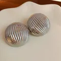 Close-up detail of stylish silver metallic ribbed dome stud earrings on white ceramic. - Striped / Silver
