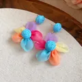 Primer plano detallado de pendientes de flores de gasa con un centro de rafia azul vibrante - Flor Multicolor / Azul