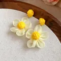 Primer plano de los pendientes de flores de rafia amarilla y gasa blanca sobre tela - Amarillo