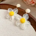 Primer plano de pendientes de margarita con pétalos de gasa blanca y rafia amarilla artesana - Flor Amarilla / Beige