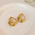 Detailed close-up view of elegant gold-plated crumpled metal stud earrings on a white saucer - Pleated Hollow Out / Gold