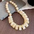 Primer plano detallado de collar de acrílico jaspeado crema con anillos dorados sobre un libro - Beige