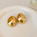 Close-up of polished golden oval metallic stud earrings displayed on a white ceramic plate - Gold Plating / Gold