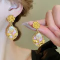 Primo piano dettagliato di orecchini vintage a camelia dorata con perle barocche e smalto. - 24# Stile Smalto Rosa Camelia