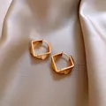 Elegant gold geometric twisted hoop earrings displayed on champagne silk fabric - 106 Earrings - Gold