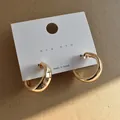 Close-up of chunky gold geometric hoop earrings on a white display card. - Gold
