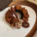 Close-up detail of leopard print bear and pom-pom decor on brown pleated fabric scrunchie - Brown