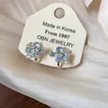 Detailed view of light blue flower clip-on earrings with pearls and crystals on display card - Clip-On Earrings / Silver-Blue
