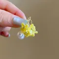Nahaufnahme von 18K vergoldeten Ohrringen mit gelben Harzblumen und Perlen im Mori-Stil - Haken-Stil / Gold-Gelb