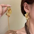 Primo piano di eleganti orecchini a petalo d'oro con lunghe nappe a catena sull'orecchio - Oro