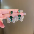 Detailed view of silver butterfly earrings featuring emerald green gemstones and rhinestones - Butterfly Emerald Rhinestone Stud Earrings / Silver Earring Post Style / Silver-Green