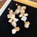 Dettaglio di orecchini pendenti in conchiglia e oro su sfondo di velluto nero. - Stile Nappa Geometrica Irregolare con Perno in Argento / Marrone oro
