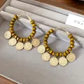 Close-up of boho hoop earrings with green wooden beads and eagle coin charms on grey tray - 33# Gold Coffee