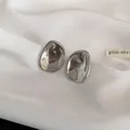 Primer plano de pendientes geométricos de metal plateado minimalistas sobre tela blanca - Geométrico irregular / Plateado