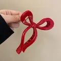 Detailed close-up showing the sleek glossy finish of a red bow-shaped hair claw clip. - Bow Streamer Style / True Red